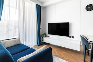 A modern living room with a sofa, a TV mounted on a white wall, and a dining area with a chair.
