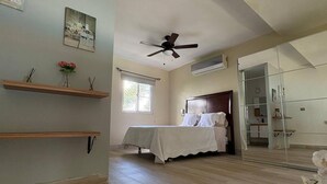 Une chambre à coucher avec un lit, un ventilateur de plafond, une fenêtre et un miroir.
