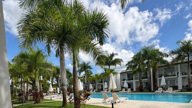 Un espace aménagé au bord de la piscine, avec des palmiers, des chaises longues et un ciel d’un bleu limpide.