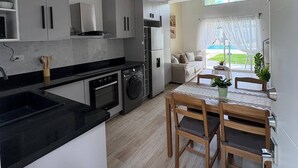 Une cuisine moderne avec des meubles gris, un plan de travail noir et un coin repas comprenant des chaises et une table en bois.