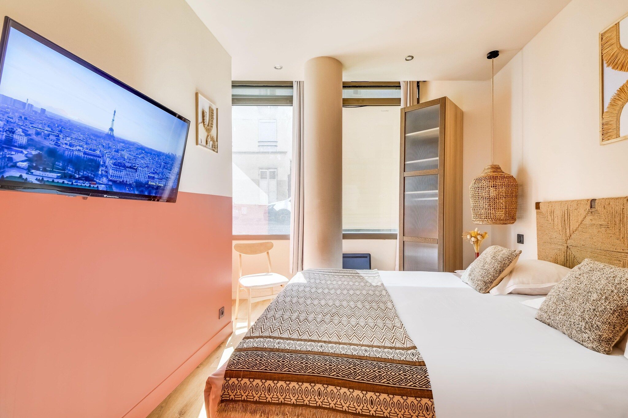 A hotel room with a bed, a desk, a television, and a large window.
