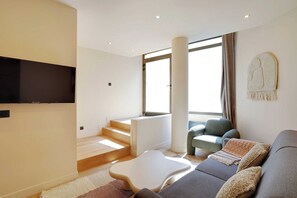 Ein modernes Wohnzimmer mit einem Flachbildfernseher, einer Couch, einem Couchtisch und einer Treppe zu einer oberen Etage.