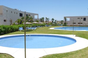 A pool area with two circular pools, surrounded by lounge chairs and umbrellas, with buildings in the background. - Sunlit Marbella Apartment Near Sea (Marbella)