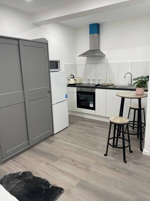 A modern kitchen with white cabinetry, a built-in oven, a microwave, and a gas stove. There are two stools and a small table with a potted plant.
