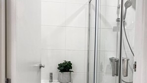Une salle de bain moderne avec une douche à parois de verre, un lavabo blanc agrémenté d’une plante en pot et un meuble de rangement.