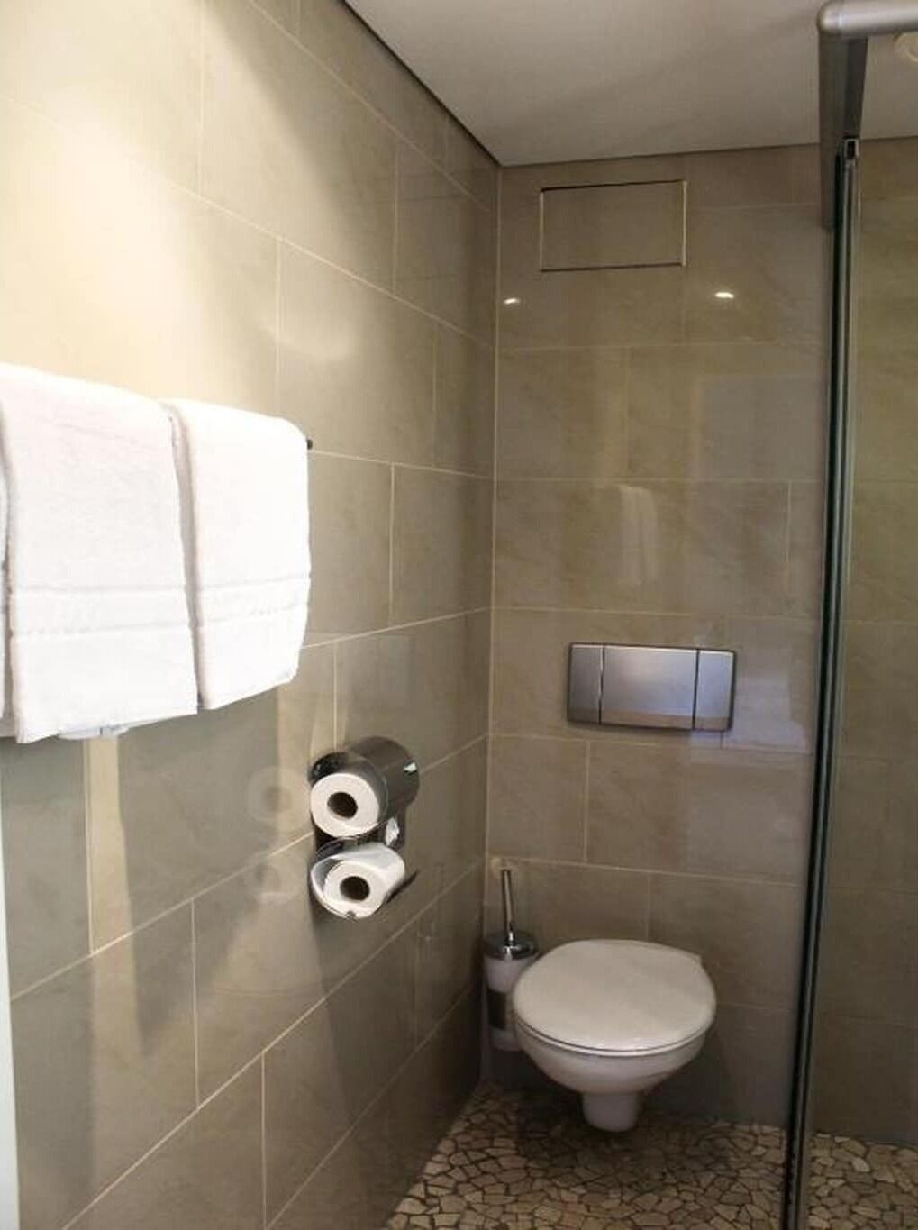 A bathroom with a toilet, a towel rack with towels, and toilet paper.