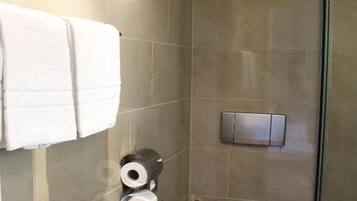 A bathroom with a toilet, a towel rack with towels, and toilet paper.
