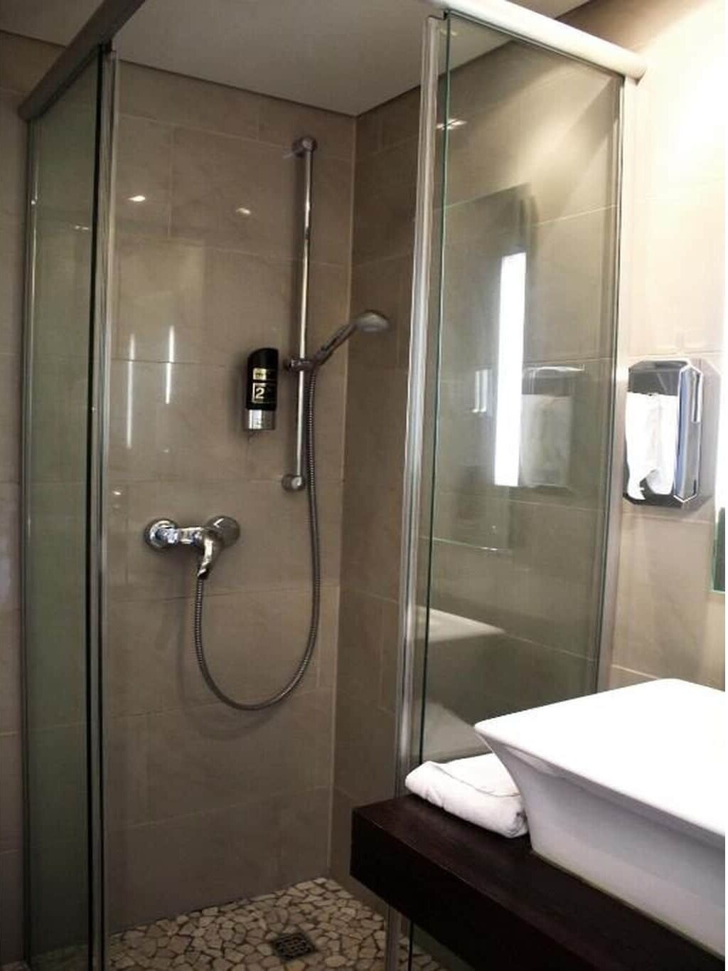 Un espace douche entièrement vitré, doté d’un pommeau de douche à main et d’un panneau de commande fixé au mur.