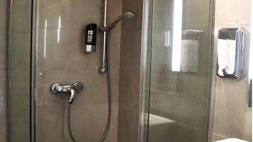 Un espace douche entièrement vitré, doté d’un pommeau de douche à main et d’un panneau de commande fixé au mur.