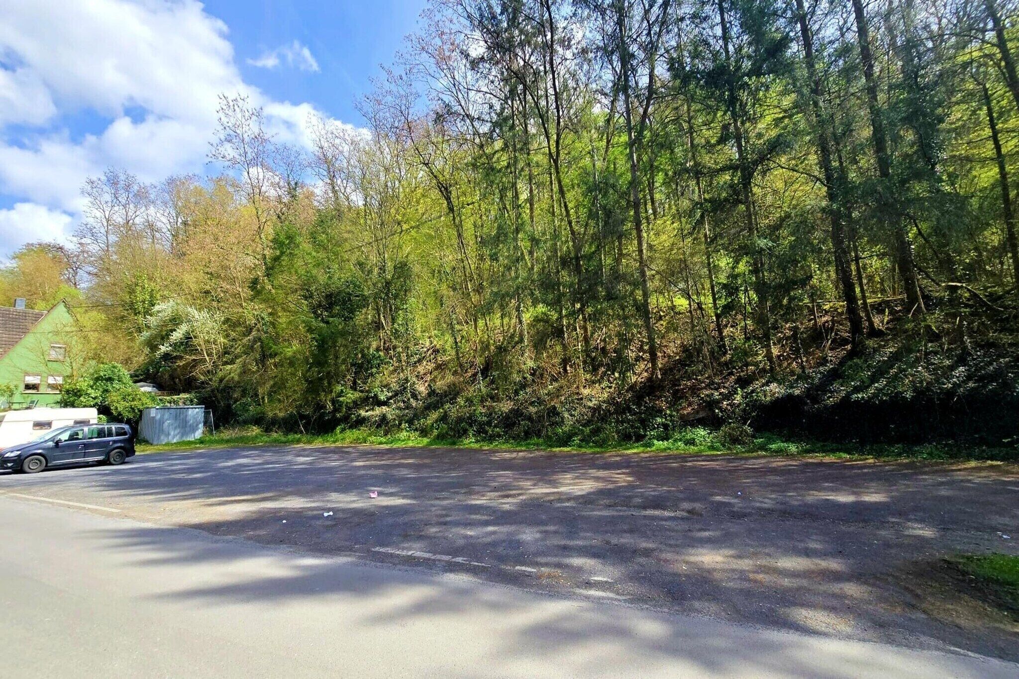 Eine Straße mit einem geparkten Auto, einem grünen Gebäude und einem dichten Wald.