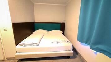 A small, single-bed room with a teal headboard, white bedding, and a blue curtain.