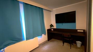 Ein Zimmer mit Bett, Schreibtisch, Stuhl, Fernseher und einem fenster mit Vorhängen.