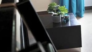 Ein modernes Zimmer mit einem dunkelgrauen Sofa, einem kleinen Tisch mit zwei Topfpflanzen und einem Glas, sowie einem Fenster mit blauen Vorhängen.