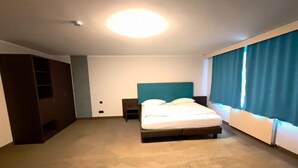 Quarto de hotel com cama, mesa de cabeceira, guarda-roupa e janela com cortinas.