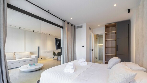 Una habitación de hotel moderna con una cama grande, una mesita de centro redonda, un sofá y un vestidor.