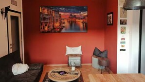 Un salon chaleureux avec un mur rouge, un tableau représentant un paysage urbain, un canapé, une table basse et une lampe.