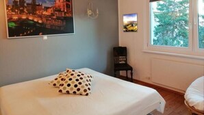 Une chambre à coucher comprenant un lit, une chaise, une fenêtre donnant sur des arbres et deux tableaux accrochés au mur.