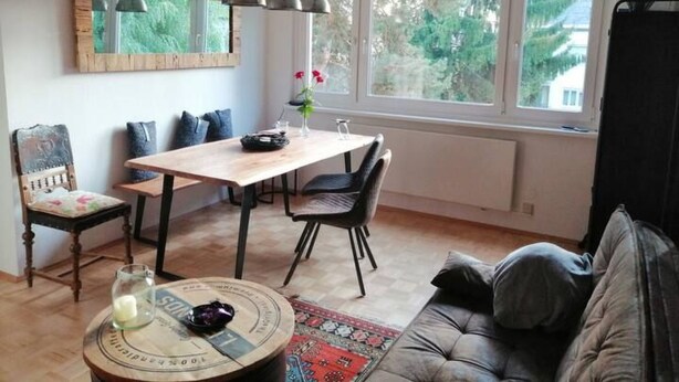 Un salon chaleureux comprenant un coin repas, un canapé, une table basse et une vue sur la verdure environnante.