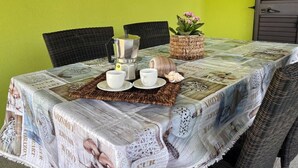 Une table dressée avec une cafetière, des tasses, des soucoupes, un objet décoratif et une plante en pot, le tout placé devant un mur vert.