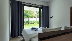 A hotel room with a bed, a wooden headboard, and a view of a garden through a sliding glass door. - Pulau Indah Lombok Hotel (Kuta)