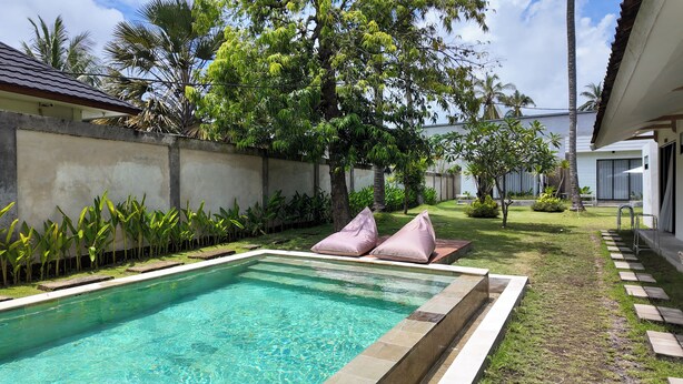 A rectangular swimming pool with a clear blue water surface, surrounded by a low stone wall and a grassy area with a few plants. - Pulau Indah Lombok Hotel (Kuta)