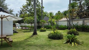 A well-maintained garden with a pool, palm trees, and a covered seating area. - Pulau Indah Lombok Hotel (Kuta)