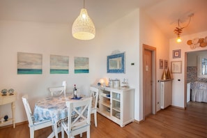 A dining area with a table set for four, a white cabinet with glass doors, and a hanging light fixture. - The Nest (Castelletto)