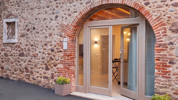 A stone building with a large arched entrance, a number '6' sign, and a small planter with plants. - Bohemia Apartment (Calmasino)