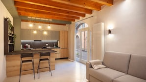 A modern kitchen with wooden beams, a dining area with two bar stools, and a sofa in a bright living space. - Bohemia Apartment (Calmasino)