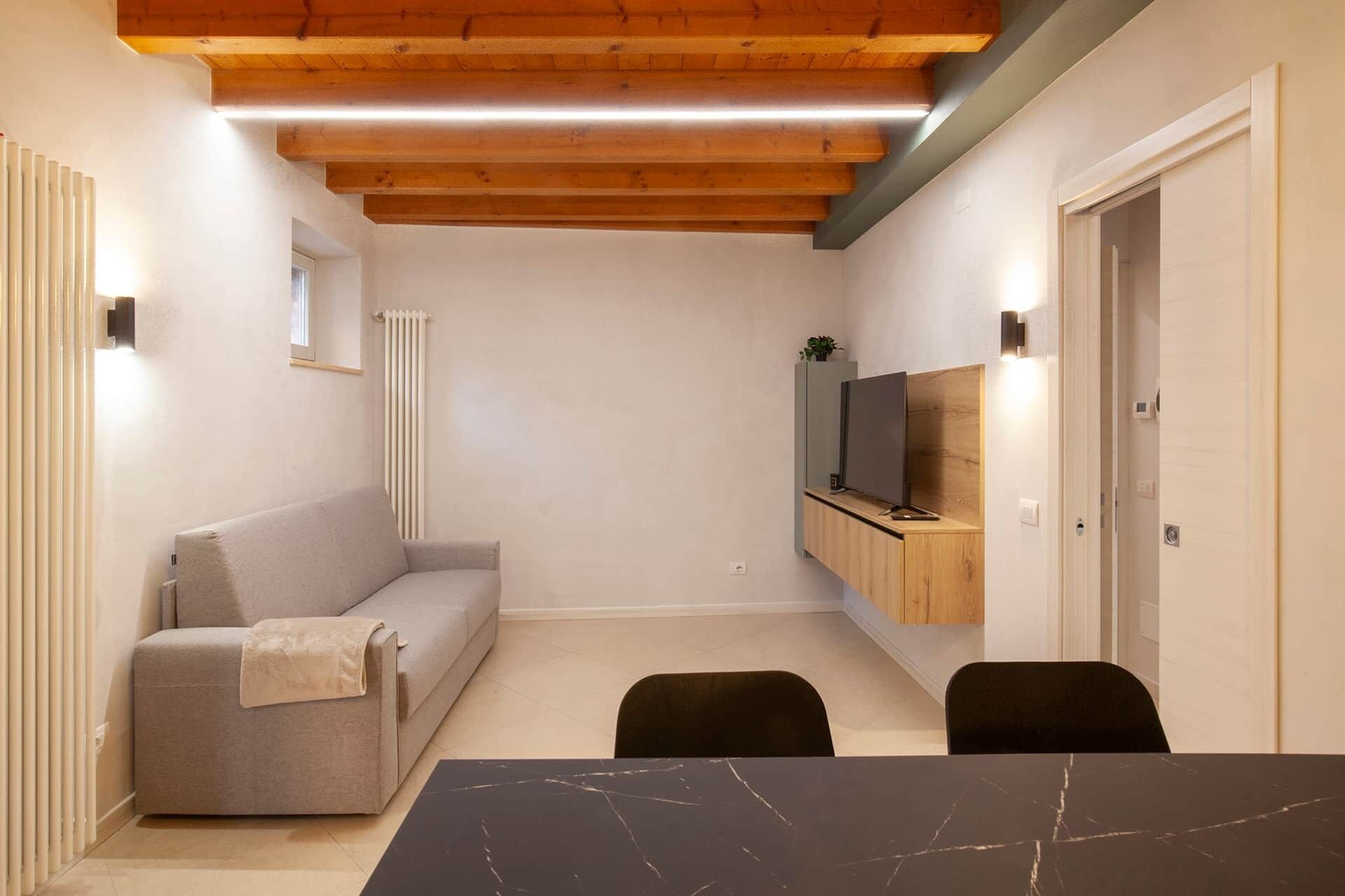 A compact living space with a sofa, a dining table, and a TV mounted on a wooden cabinet.