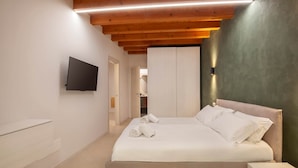 A bedroom with a bed, a TV mounted on the wall, and a wooden ceiling. - Bohemia Apartment (Calmasino)