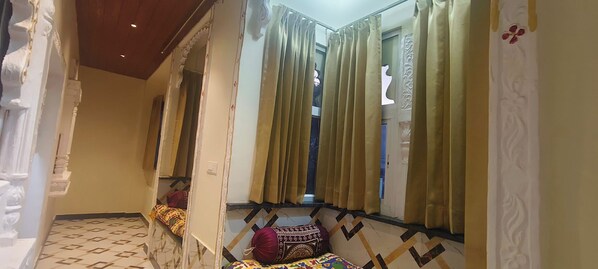 A hallway with patterned flooring, a bed with a colorful blanket, and curtains. - Shree ji palace (Udaipur)