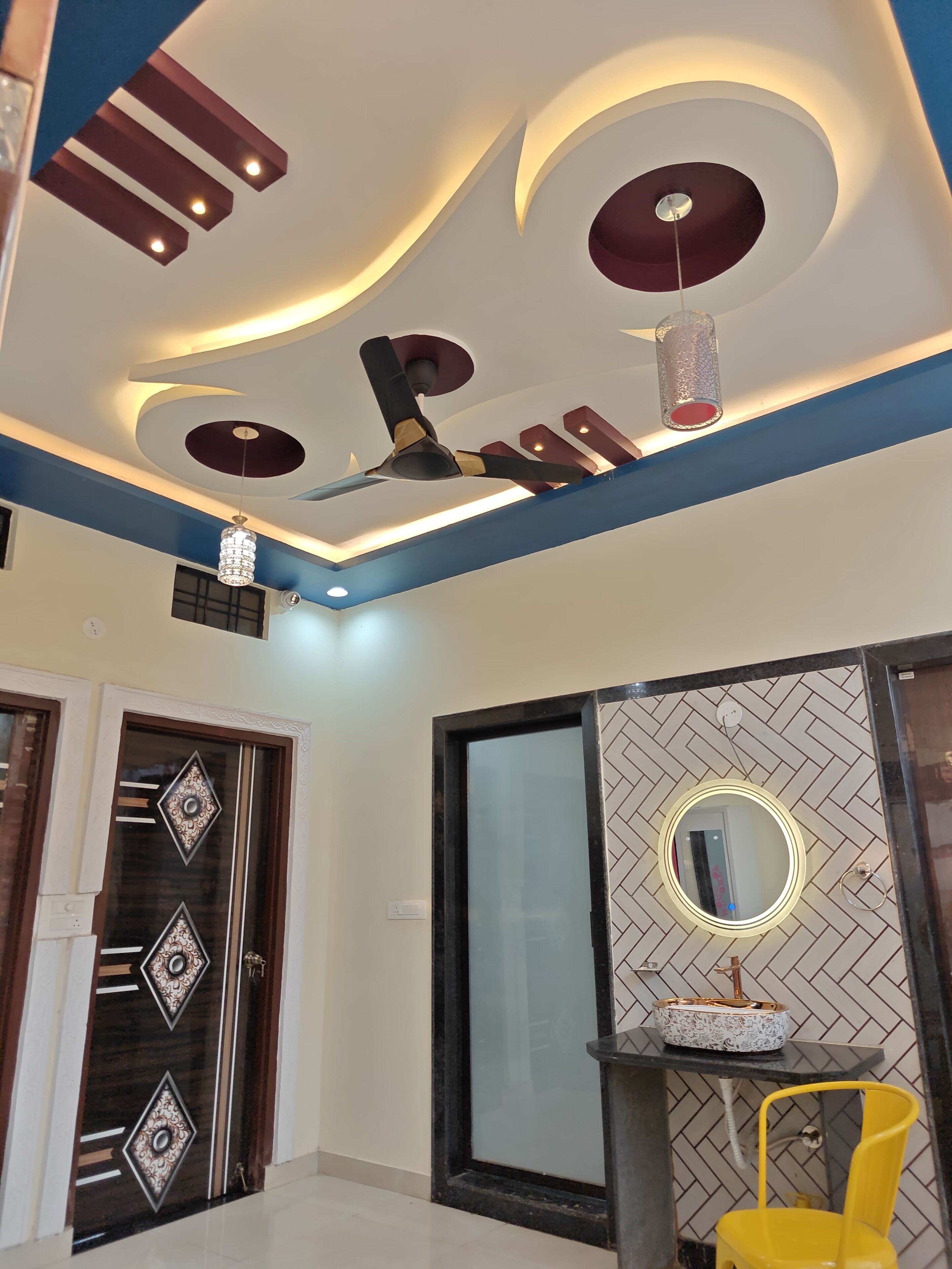 A modern interior with a ceiling fan, decorative lighting, a mirror, and a yellow chair.