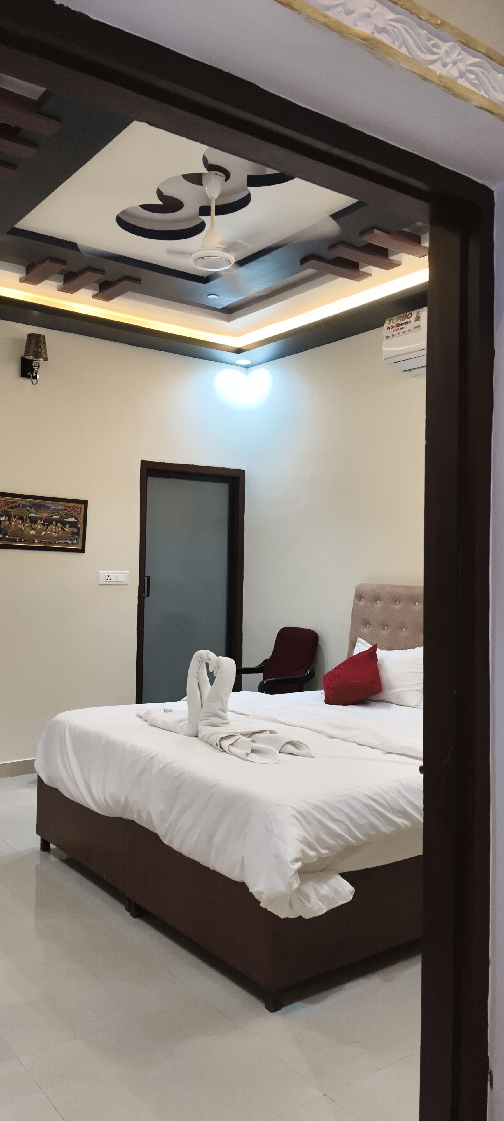A bedroom with a bed, a red chair, a door, and a ceiling with a light fixture.