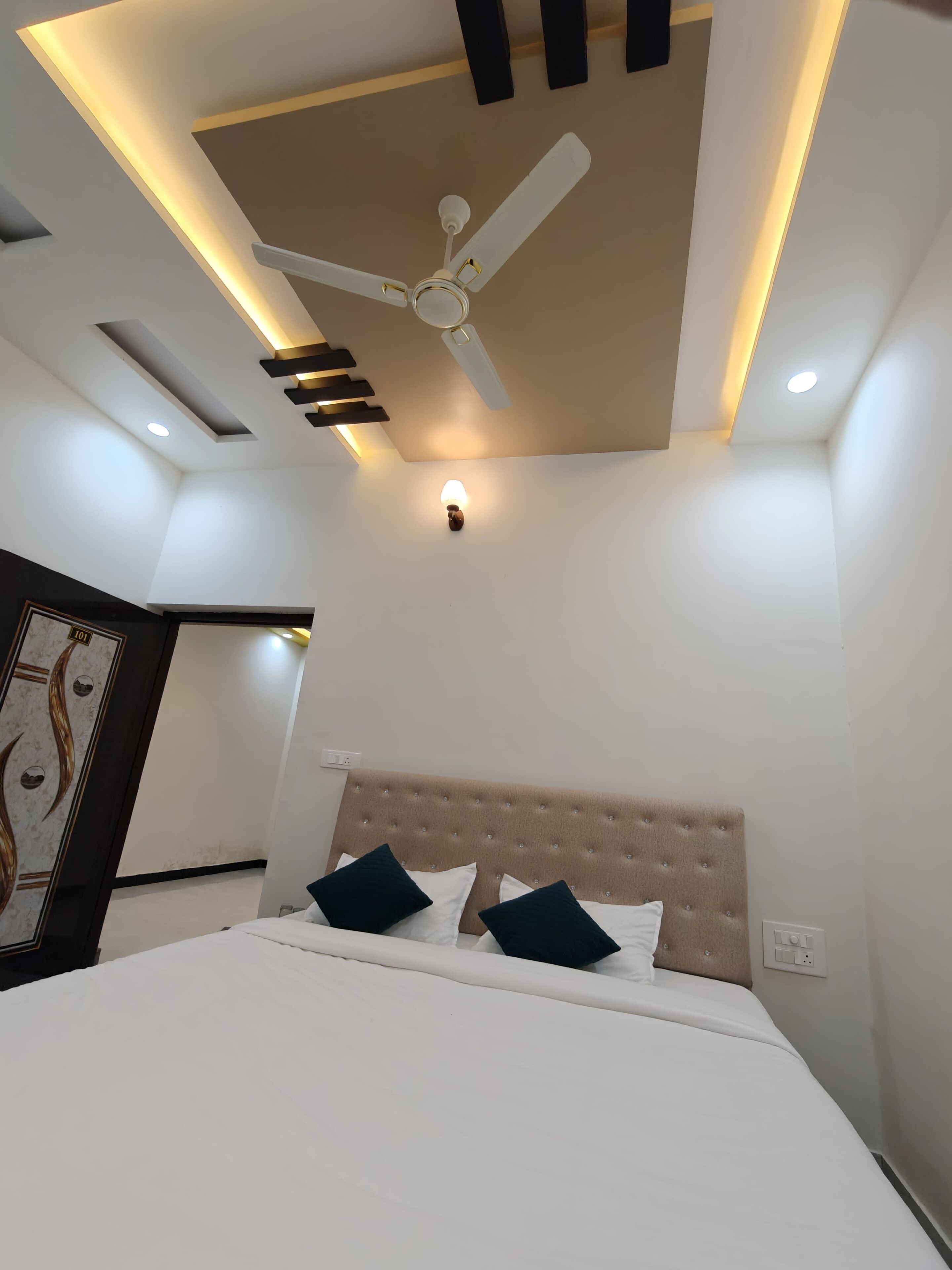 Une chambre à coucher moderne, équipée d’un lit, d’un ventilateur de plafond, d’un éclairage encastré et d’un luminaire fixé au mur.