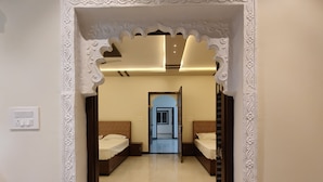 A hallway with two beds, a door leading to another room, and a light switch on the wall. - Shree ji palace  (Udaipur)