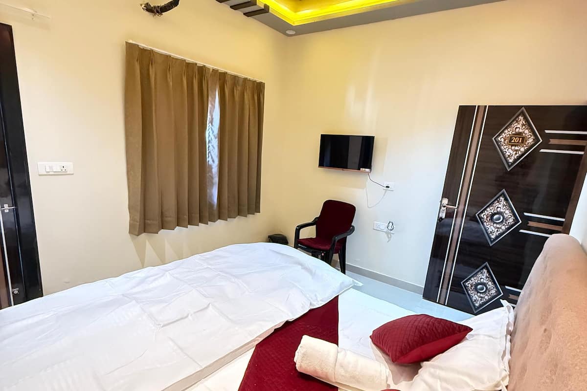 A hotel room with a bed, a ceiling fan, a TV, a door with a number plate, and a window with curtains.
