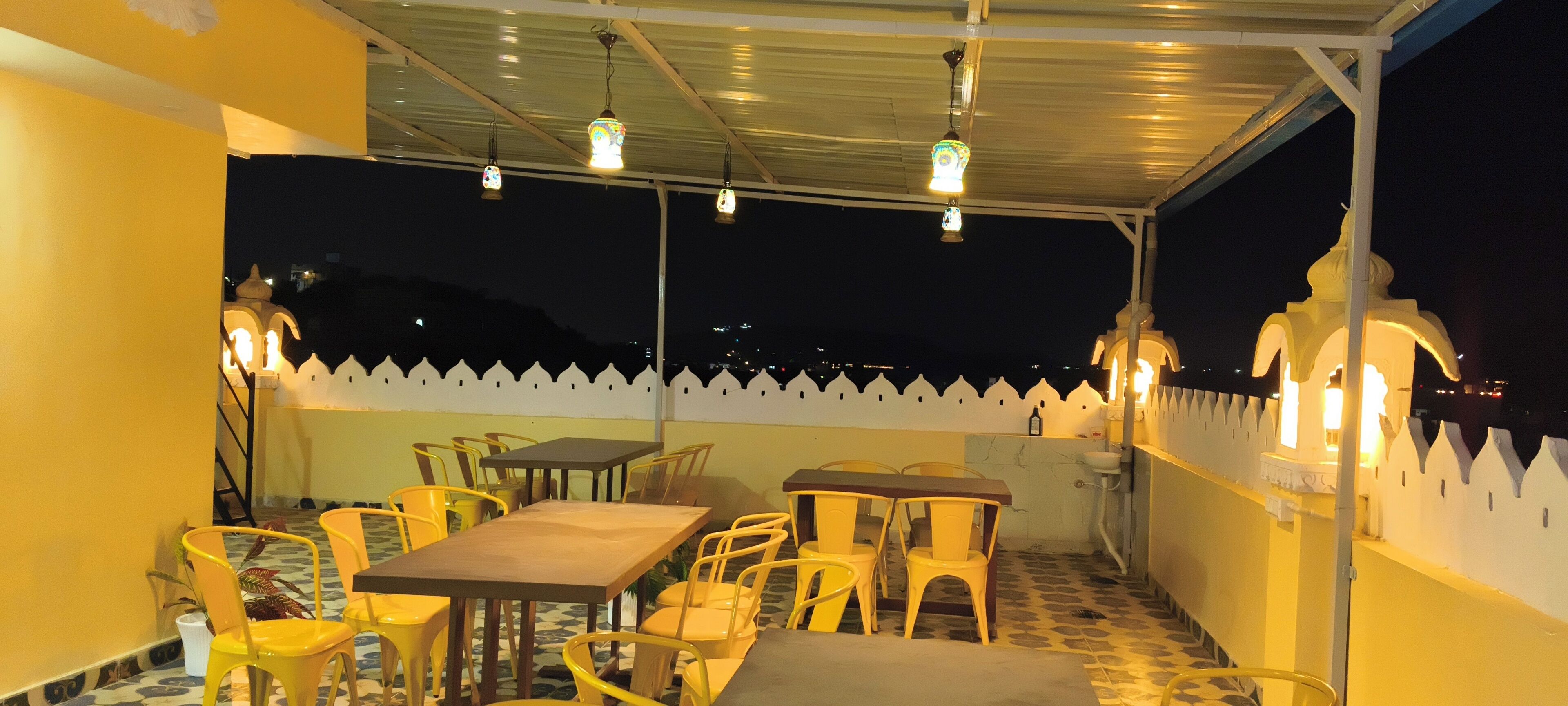 A covered outdoor seating area with tables and chairs, decorative lights, and a white picket fence.