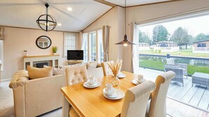 A cozy living room with a wooden dining table, beige sofas, and a TV. - Host & Stay | Huckleberry Lodge (Pocklington)