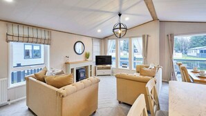 A cozy living room with a fireplace, comfortable sofas, a dining area, and large windows offering a view of the outside. - Host & Stay | Huckleberry Lodge (Pocklington)