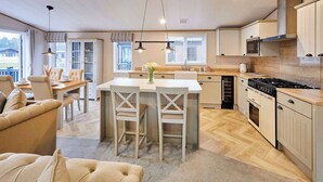 A spacious kitchen with a central island, wooden cabinets, and a dining area with a sofa and chairs. - Host & Stay | Huckleberry Lodge (Pocklington)