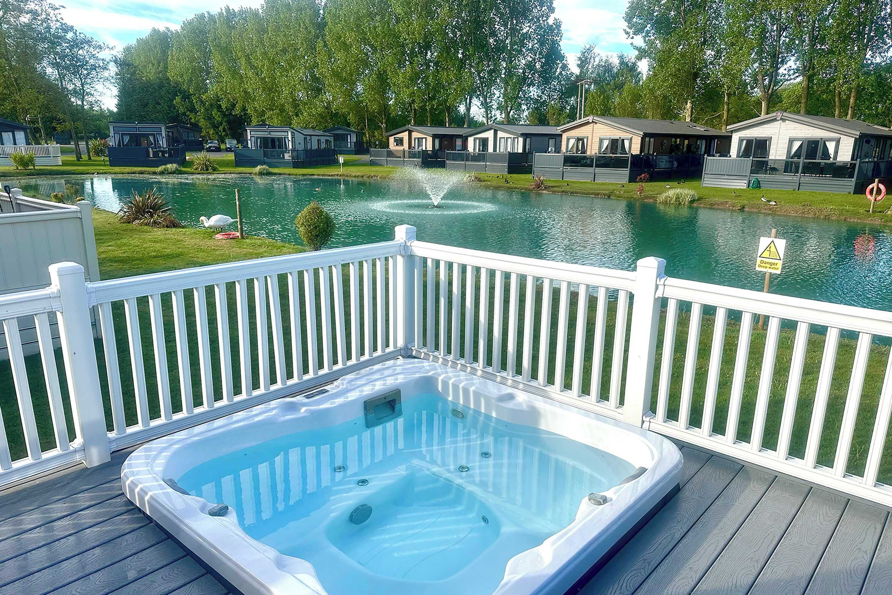 Uma banheira de hidromassagem em um deck com um lago e casas ao fundo.