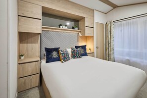 A bedroom with a bed, built-in shelving, a bedside table, and a window with curtains. - Host & Stay | Honey Bee Lodge (Pocklington)