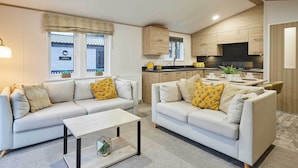 Ein modernes Wohnzimmer mit zwei Sofas, einem Couchtisch und einer Küchenzeile mit Holzschränken und einem schwarzen Herd.