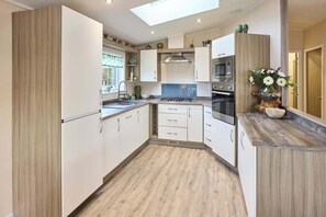 A modern kitchen with white cabinets, a skylight, a built-in oven, and a microwave. - Host & Stay | Take Time Out (Pocklington)