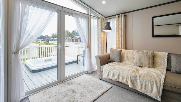 Un salon confortable avec un canapé, une grande fenêtre avec des rideaux, un jacuzzi et une vue sur une terrasse et des maisons.