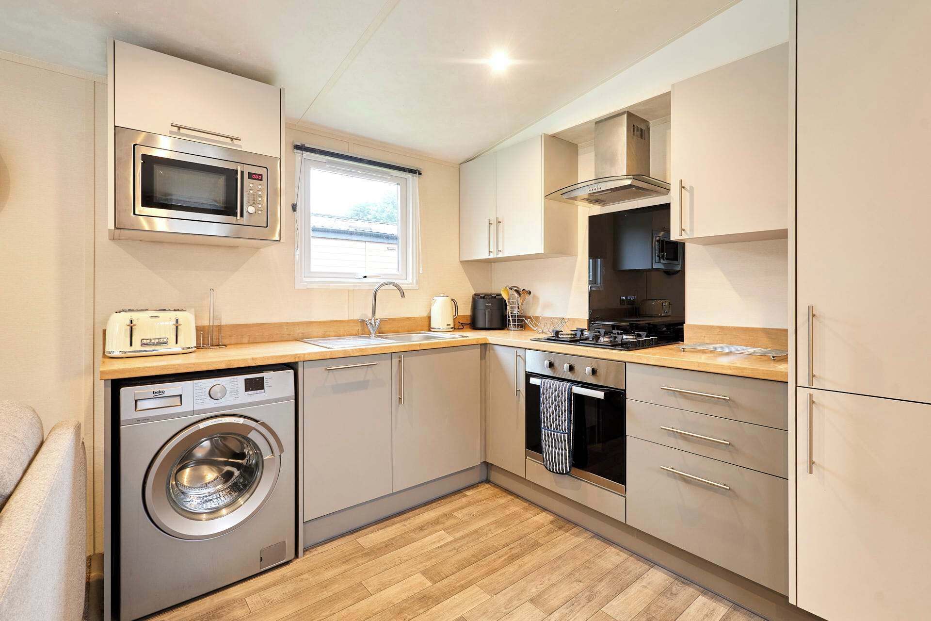A compact kitchen with a washing machine, microwave, oven, and a window providing natural light.