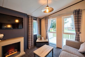 A cozy living room with a fireplace, a sofa, a table, and plaid curtains. - Host & Stay | Oakwood Lodge (Pocklington)