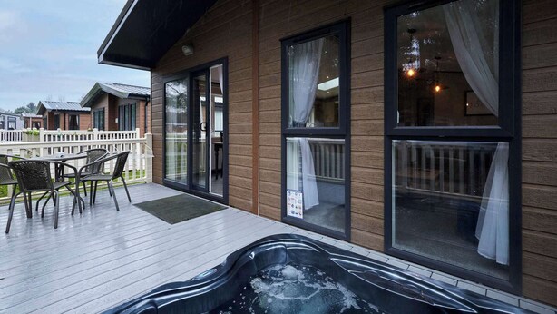 En byggnad av trä med ett bubbelbad på terrassen, skjutdörrar i glas och utsikt över andra byggnader.