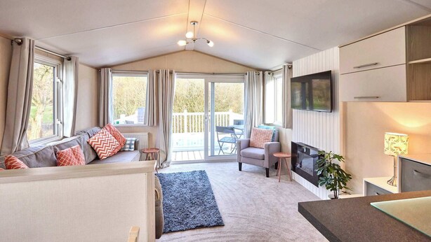 En hyggelig opholdsstue med sofa, lænestol og fjernsyn. Der er en balkon med bord og stole.